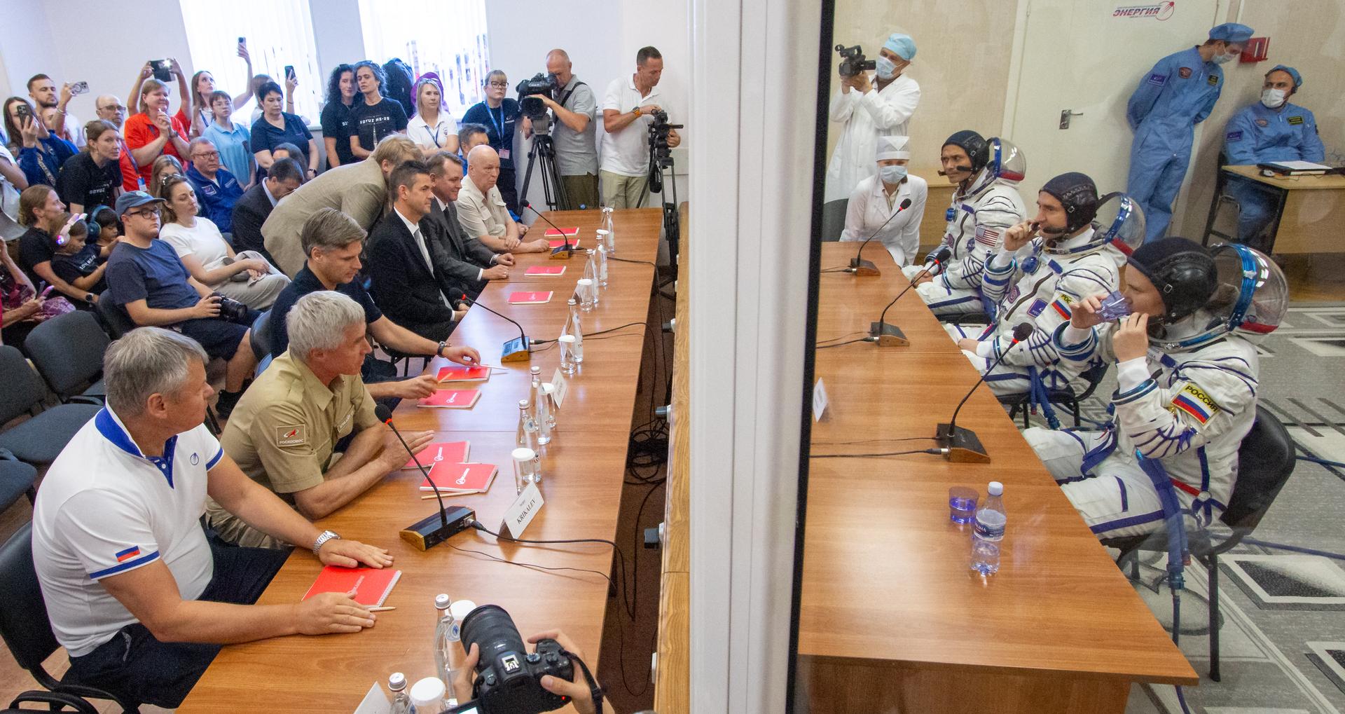 Expedition 75 Roscosmos cosmonaut Anna Kikina, foreground left, Roscosmos cosmonaut Pyotr Dubrov, and NASA astronaut Anil Menon, background right, talk with Roscosmos Director of Human Spaceflight Programs Sergei Krikalev, seated 2nd from left, Roscosmos Director General Dmitry Bakanov, seated 3rd from left, NASA Administrator Jared Isaacman, and NASA Deputy Administrator Matt Anderson, 5th from left, after having their Russian Sokol suits pressure checked as they prepare for their Soyuz launch to the International Space Station Tuesday, July 14, 2026 in Baikonur, Kazakhstan. Photo Credit: (NASA/Victor Zelentsov)