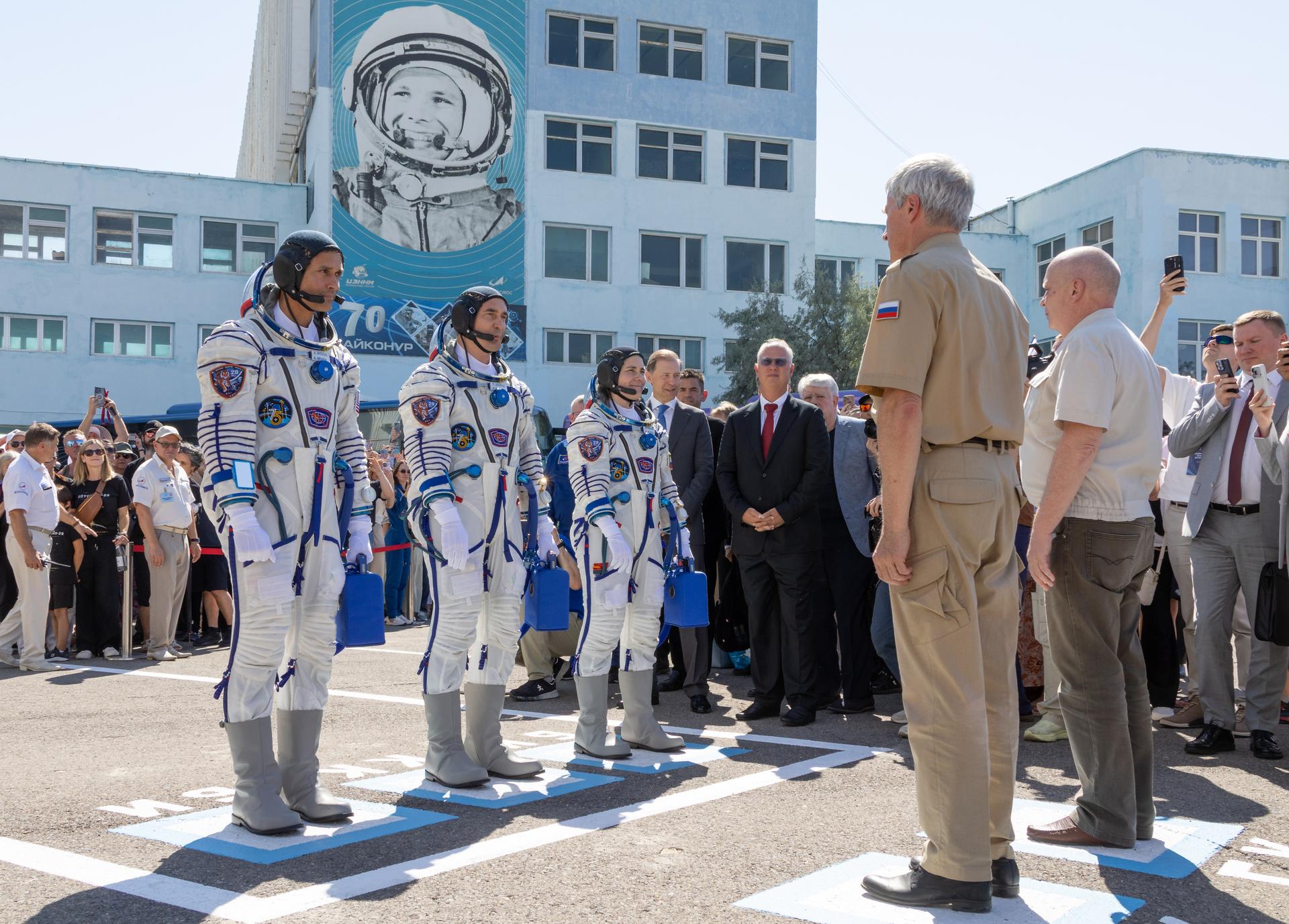Expedition 75 crewmembers: NASA astronaut Anil Menon, left, Roscosmos cosmonauts Pyotr Dubrov, and Anna Kikina, right, report to Roscosmos leadership as they depart building 254 for their Soyuz launch to the International Space Station Tuesday, July 14, 2026 in Baikonur, Kazakhstan. Photo Credit: (NASA/Victor Zelentsov)