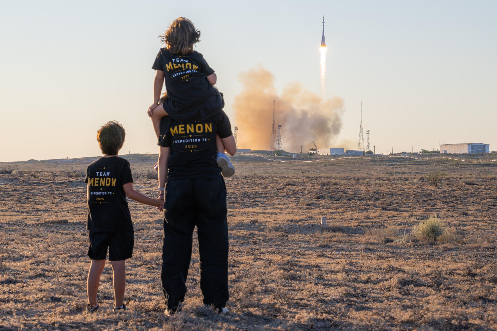 NASA astronaut candidate Anna Menon and her children watch as a Soyuz rocket launches to the International Space Station with Expedition 75 crewmembers NASA astronaut Anil Menon and Roscosmos cosmonauts Pyotr Dubrov and Anna Kikina, Tuesday, July 14, 2026, at Site 31/6 at the Baikonur Cosmodrome in Kazakhstan. The trio lifted off for the Soyuz MS-29 mission at 7:47 p.m. local time to begin their long-duration stay aboard the orbital outpost. Photo Credit: (NASA/John Kraus)