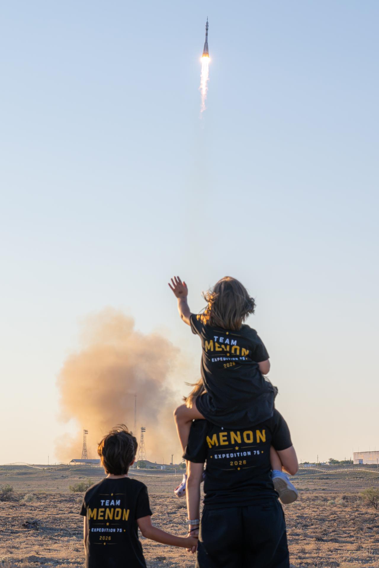NASA astronaut candidate Anna Menon and her children watch as a Soyuz rocket launches to the International Space Station with Expedition 75 crewmembers NASA astronaut Anil Menon and Roscosmos cosmonauts Pyotr Dubrov and Anna Kikina, Tuesday, July 14, 2026, at Site 31/6 at the Baikonur Cosmodrome in Kazakhstan. The trio lifted off for the Soyuz MS-29 mission at 7:47 p.m. local time to begin their long-duration stay aboard the orbital outpost. Photo Credit: (NASA/John Kraus)