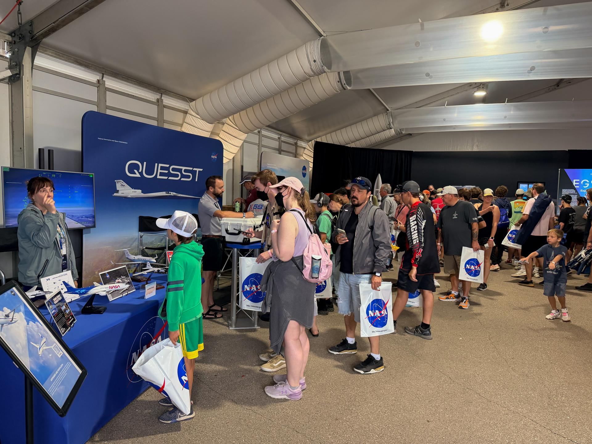 A line of visitors work their way through the exhibits and stop by the Quesst table in the NASA pavilion at the 2026 Experimental Aircraft Association (EAA) AirVenture air show in Oshkosh, Wisconsin, on Saturday, July 25, 2026.