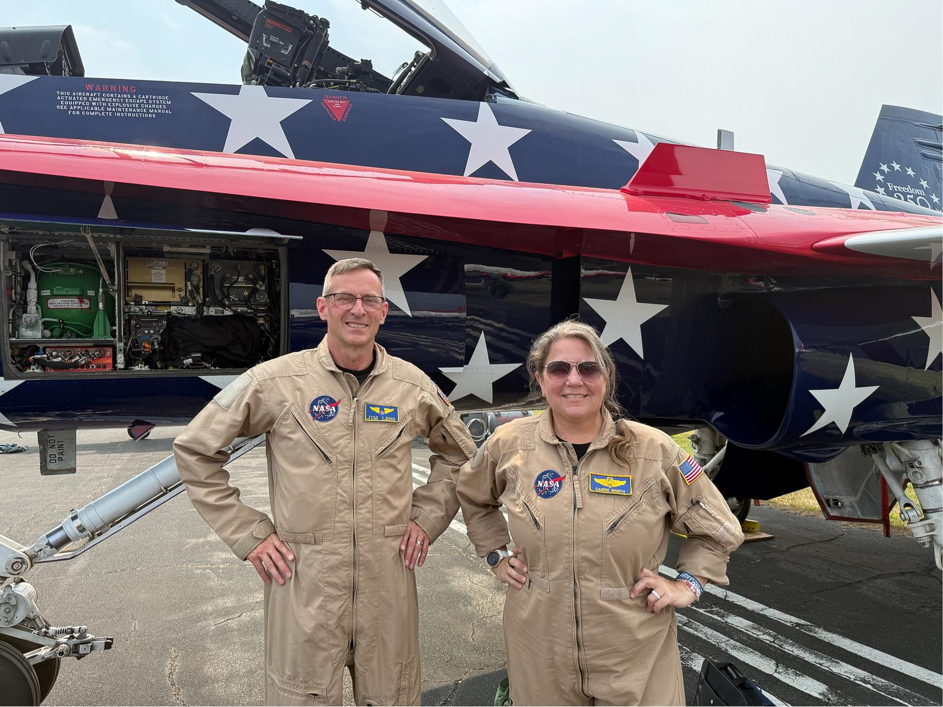 NASA test pilot Jim “Clue” Less and NASA research pilot Carrie Worth stand in front of an F/A-18 Hornet with special patriotic livery celebrating America 250, including navy blue-and-white star covered fuselages and red-and-white striped wings at the 2026 Experimental Aircraft Association (EAA) AirVenture air show in Oshkosh, Wisconsin, on Saturday, July 26, 2026.