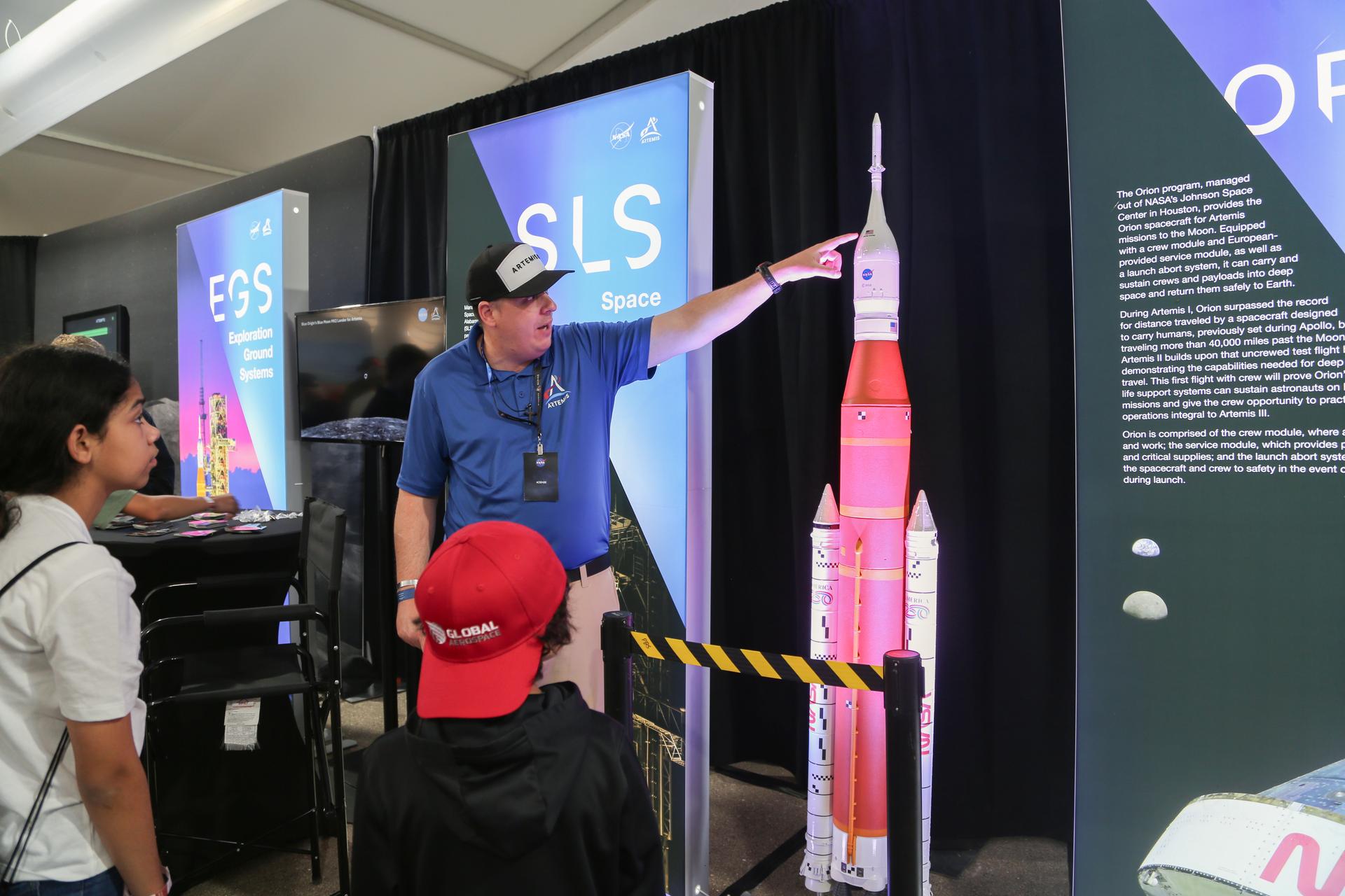NASA Communications Strategist Will Bryan shows visitors an Orion spacecraft model at the Artemis display in the NASA pavilion at the 2026 Experimental Aircraft Association (EAA) AirVenture air show in Oshkosh, Wisconsin, Monday, July 20, 2026.