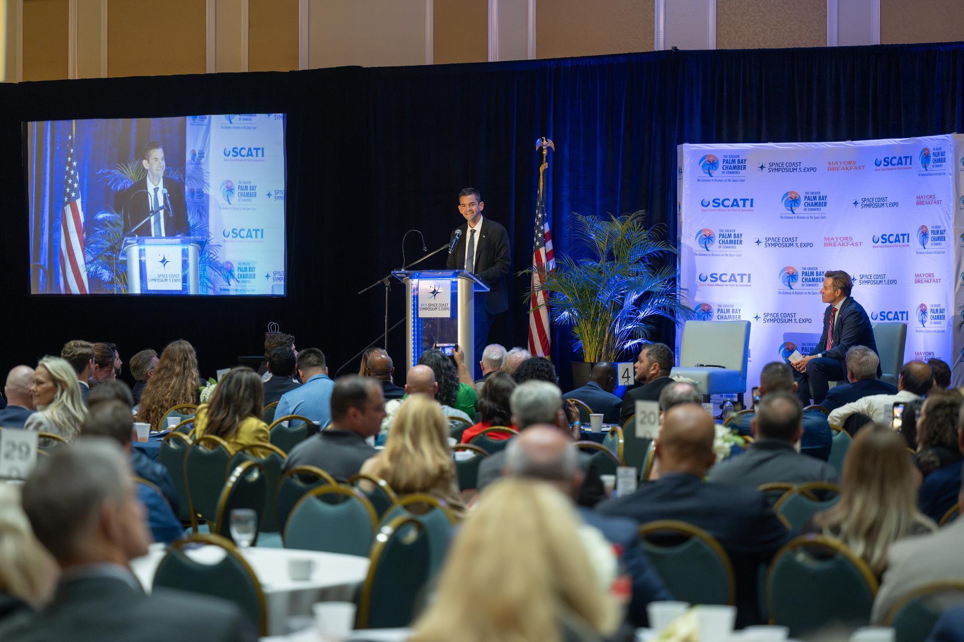 NASA Administrator Jared Isaacman, center, participates in a fireside chat with U.S. Rep. Mike Haridopolos of Florida’s 8th congressional district, right, Friday, Aug. 21, 2026, at the 8th Annual Space Coast Symposium & Expo in Cape Canaveral, Fla. Photo Credit: (NASA/John Kraus)