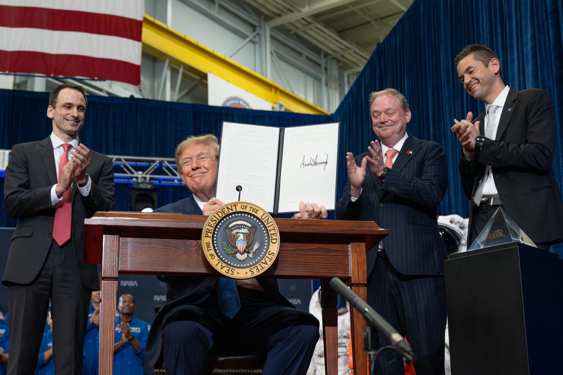 President Donald Trump presents an executive order establishing the United States Space Academy during an event to award the Congressional Space Medal of Honor to the Artemis II crew as Michael Kratsios, director of the Office of Science and Technology Policy, left; Kevin Hassett, director of the National Economic Council, third from left; and NASA Administrator Jared Isaacman, right, applaud, Friday, Aug. 28, 2026, at NASA's Johnson Space Center in Houston, Texas. The Artemis II crew completed their approximately ten-day mission around the Moon in April 2026 and are the 31st, 32nd, 33rd, and 34th astronauts to receive the award. Photo Credit: (NASA/John Kraus)