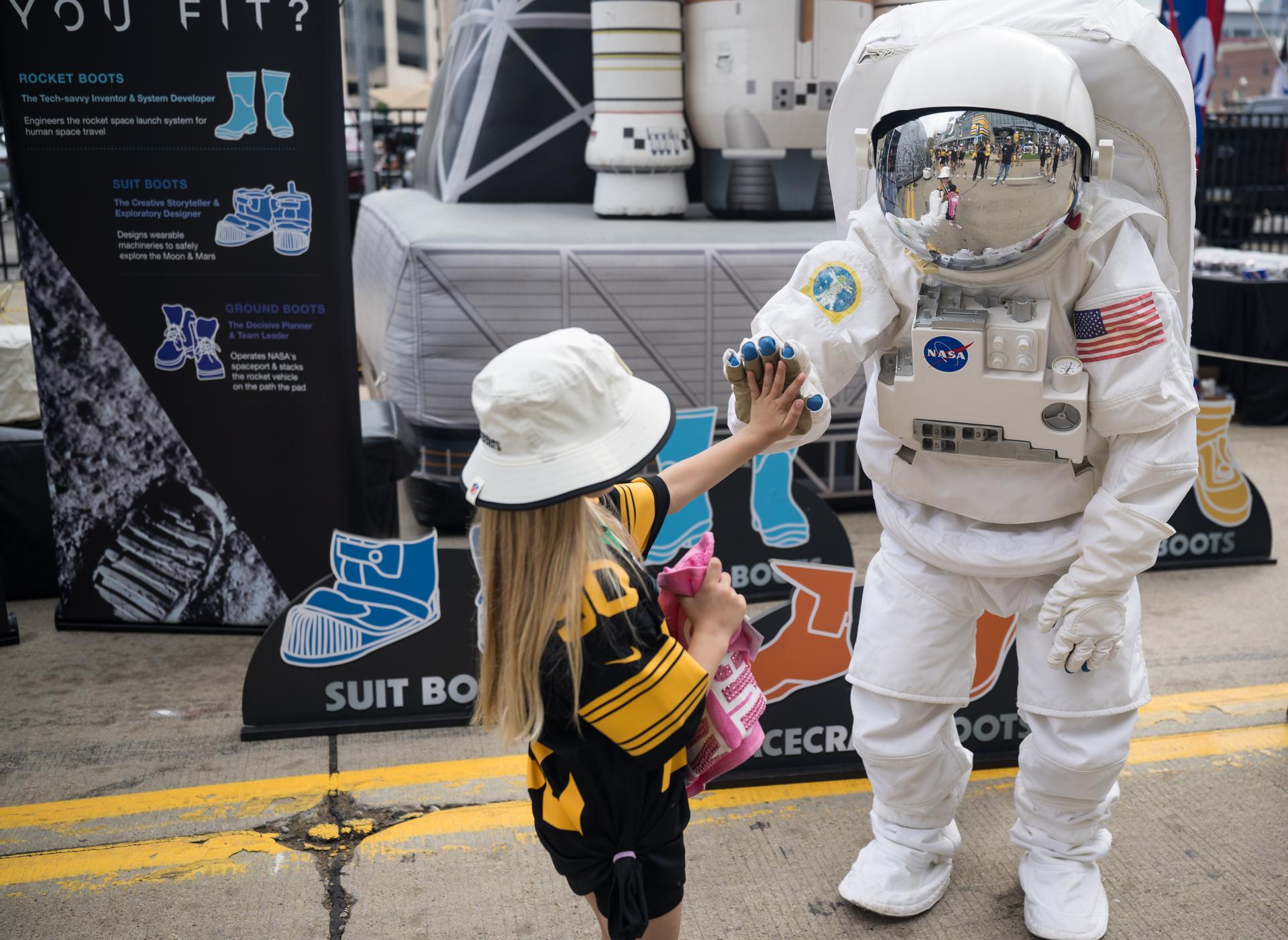 A young fan high fives the astronaut in the NASA Experience Zone at an NFL game between the Pittsburgh Steelers and the Atlanta Falcons at Acrisure Stadium, Sunday, Sept. 13, 2026, in Pittsburgh, Pennsylvania. NASA’s engagement at NFL games is part of the agency's Inspiration Tour, aimed at strengthening connections between NASA and its partners and showcasing innovation in air and space in the lead up to the MAX POWER aerospace technology expo and airshow at the agency's Kennedy Space Center in early November. Photo Credit: (NASA/Aubrey Gemignani)