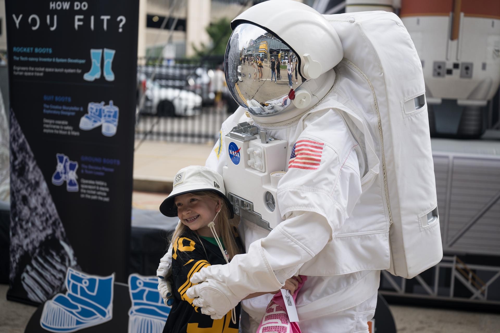A young fan poses for a photo with the astronaut in the NASA Experience Zone at an NFL game between the Pittsburgh Steelers and the Atlanta Falcons at Acrisure Stadium, Sunday, Sept. 13, 2026, in Pittsburgh, Pennsylvania. NASA’s engagement at NFL games is part of the agency's Inspiration Tour, aimed at strengthening connections between NASA and its partners and showcasing innovation in air and space in the lead up to the MAX POWER aerospace technology expo and airshow at the agency's Kennedy Space Center in early November. Photo Credit: (NASA/Aubrey Gemignani)