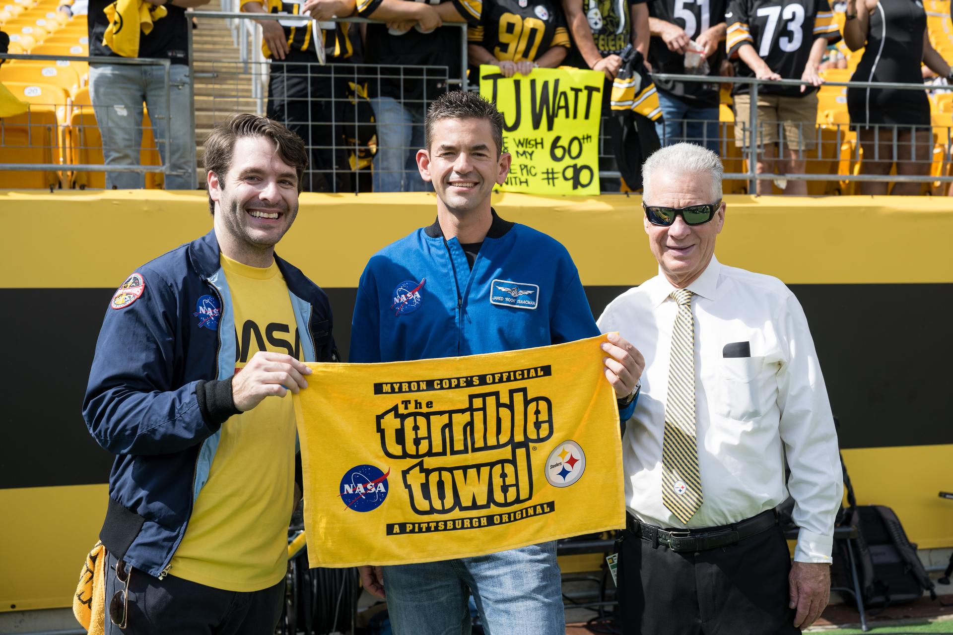 Anthony Vareha, NASA Flight Director, left, and NASA Administrator Jared Isaacman, center, receive a “Terrible Towel” from Art Rooney II, owner of the Pittsburgh Steelers, right, at an NFL game between the Steelers and the Atlanta Falcons at Acrisure Stadium, Sunday, Sept. 13, 2026, in Pittsburgh, Pennsylvania. NASA’s engagement at NFL games is part of the agency's Inspiration Tour, aimed at strengthening connections between NASA and its partners and showcasing innovation in air and space in the lead up to the MAX POWER aerospace technology expo and airshow at the agency's Kennedy Space Center in early November. Photo Credit: (NASA/Aubrey Gemignani)