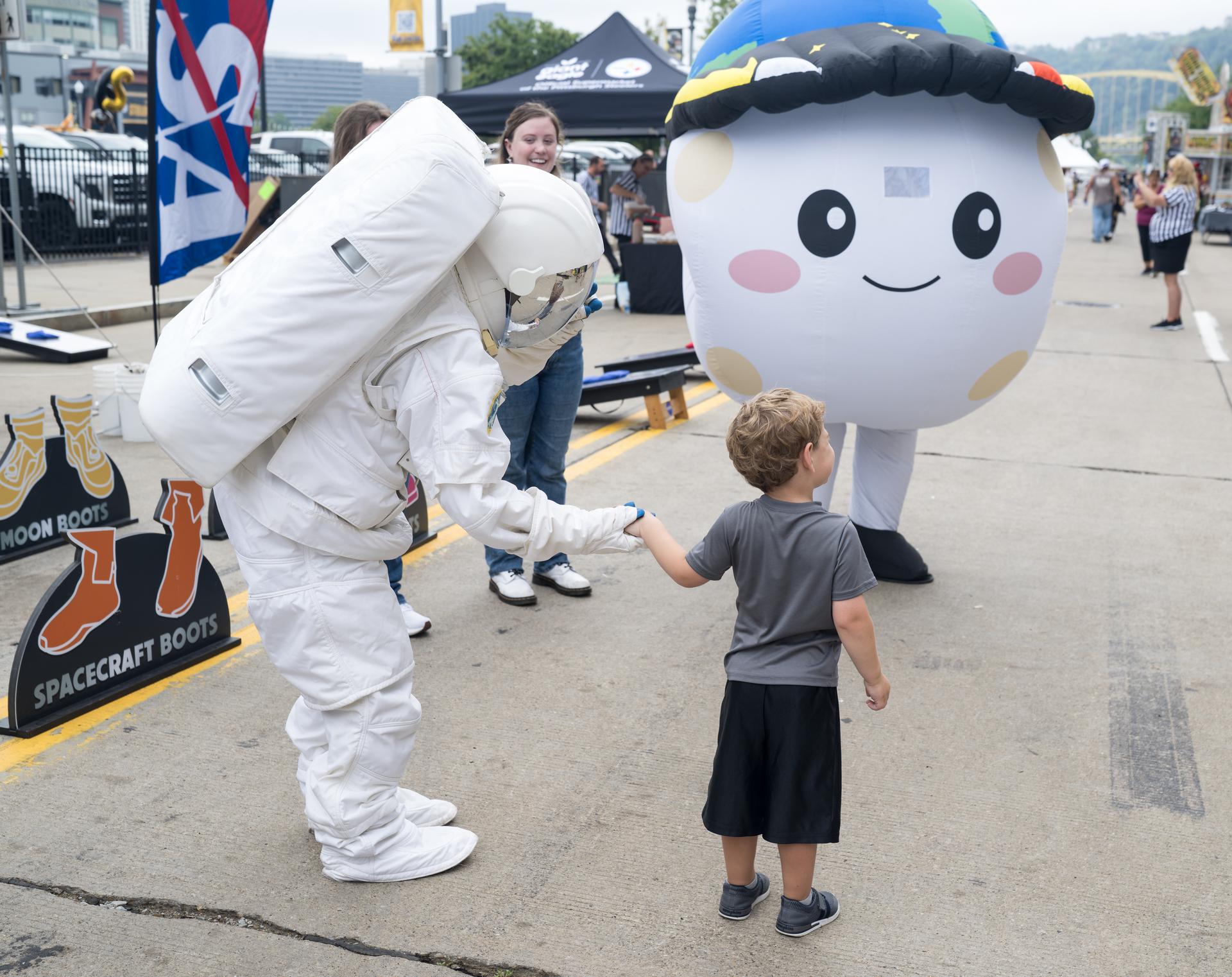 A young fan holds hands with an astronaut while Rise, the zero gravity indicator from the Artemis II mission stands by in the NASA Experience Zone at an NFL game between the Pittsburgh Steelers and the Atlanta Falcons at Acrisure Stadium, Sunday, Sept. 13, 2026, in Pittsburgh, Pennsylvania. NASA’s engagement at NFL games is part of the agency's Inspiration Tour, aimed at strengthening connections between NASA and its partners and showcasing innovation in air and space in the lead up to the MAX POWER aerospace technology expo and airshow at the agency's Kennedy Space Center in early November. Photo Credit: (NASA/Aubrey Gemignani)