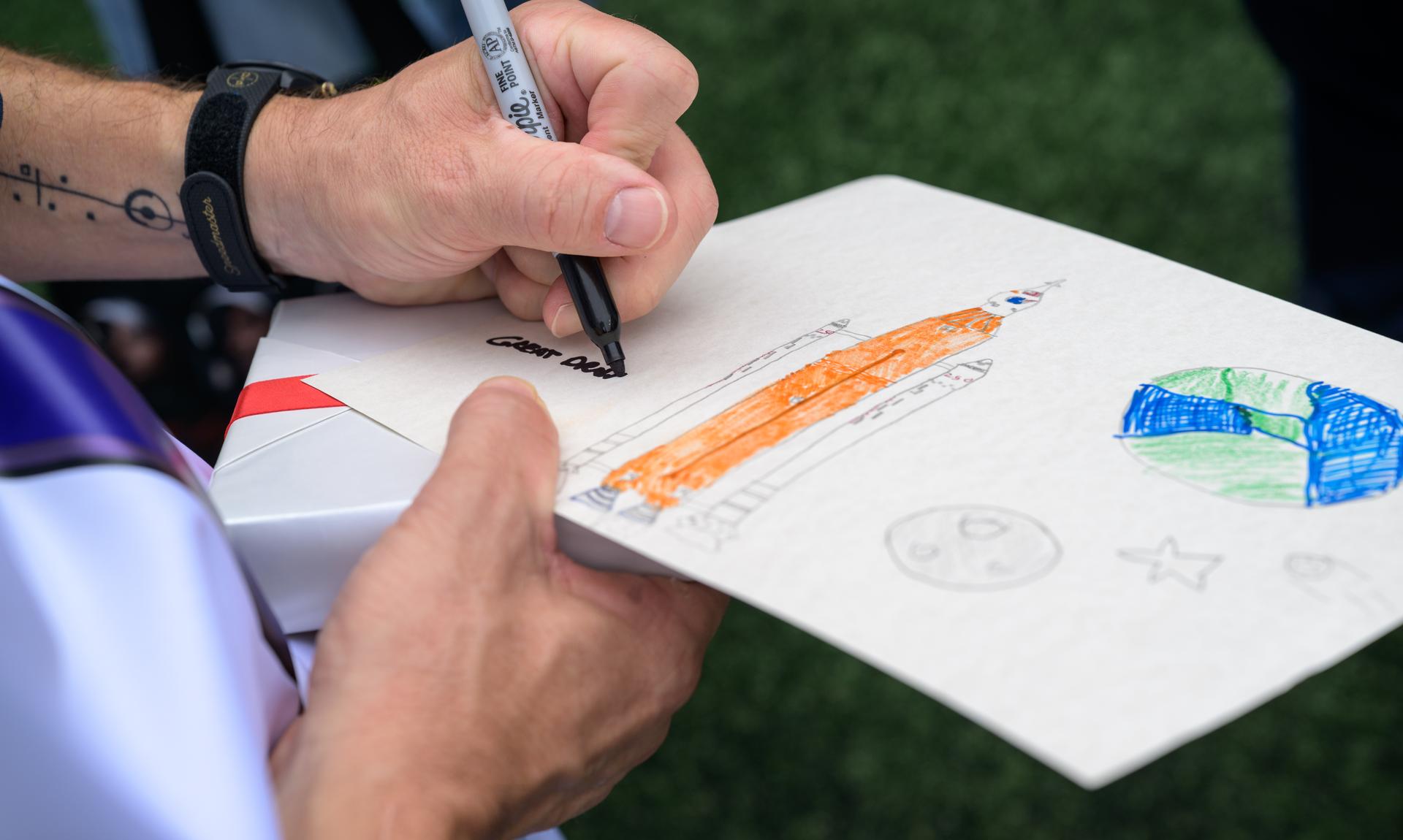 NASA astronaut and commander of the agency’s Artemis II mission, Reid Wiseman, a Baltimore native, signs artwork at an NFL game between the New Orleans Saints and the Baltimore Ravens at M&T Bank Stadium, Sunday, Sept. 20, 2026, in Baltimore. NASA’s engagement at NFL games is part of the agency's Inspiration Tour, aimed at strengthening connections between NASA and its partners and showcasing innovation in air and space in the lead up to the MAX POWER aerospace technology expo and airshow at the agency's Kennedy Space Center in early November. Photo Credit: (NASA/Bill Ingalls)