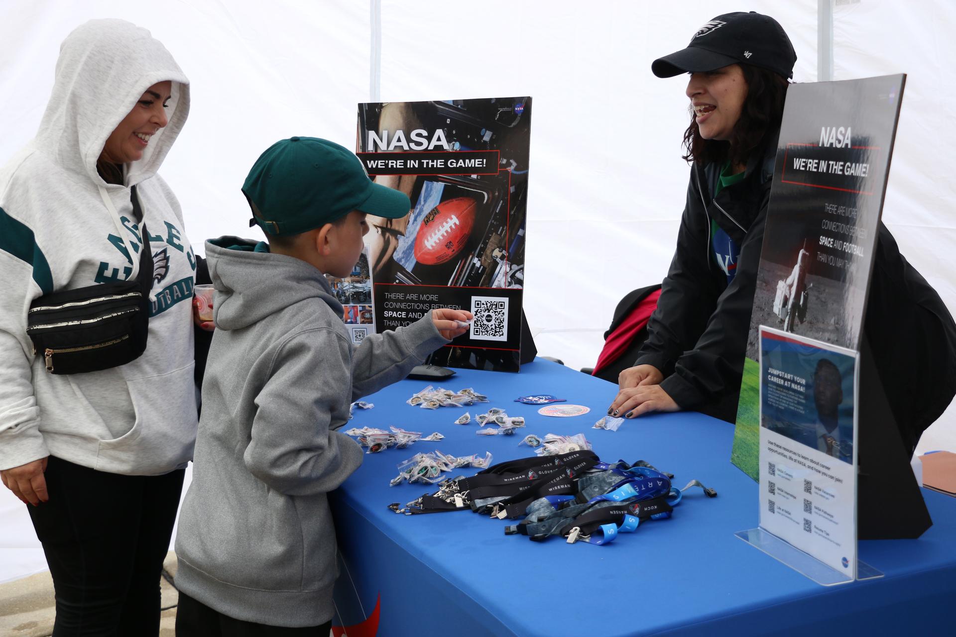 Astrophysicist Knicole Colón greets a young fan at the NASA activation as the NFL game between the Philadelphia Eagles and the Los Angeles Rams at Lincoln Financial Field on Sunday, Oct. 4, 2026, in Philadelphia. NASA’s engagement at NFL games is part of the agency's Inspiration Tour, aimed at strengthening connections between NASA and its partners and showcasing innovation in air and space in the lead up to the MAX POWER aerospace technology expo and airshow at the agency's Kennedy Space Center in early November. Photo Credit: (NASA/Thalia Patrinos)