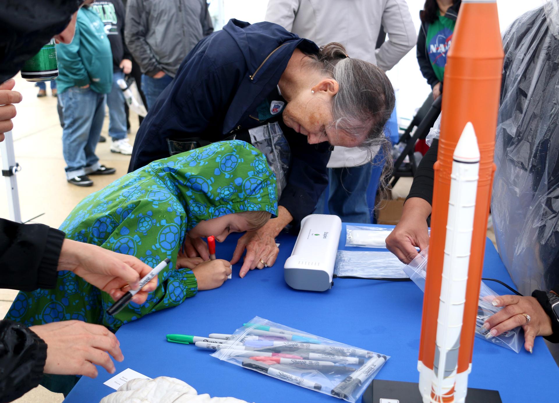 Two fans label their new luggage tag at the NASA activation at the NFL game between the Philadelphia Eagles and the Los Angeles Rams at Lincoln Financial Field on Sunday, Oct. 4, 2026, in Philadelphia. NASA’s engagement at NFL games is part of the agency's Inspiration Tour, aimed at strengthening connections between NASA and its partners and showcasing innovation in air and space in the lead up to the MAX POWER aerospace technology expo and airshow at the agency's Kennedy Space Center in early November. Photo Credit: (NASA/Thalia Patrinos)