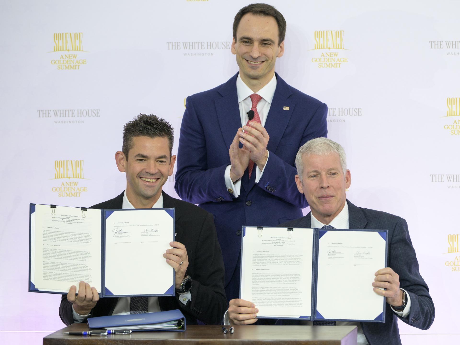 NASA Administrator Jared Isaacman, seated left, and U.S. Secretary of Energy Chris Wright, seated right, hold the signed Memorandum of Understanding, “Accelerating American Leadership in Space Nuclear Power and Propulsion”, as Director of the White House Office of Science and Technology Policy (OSTP) Michael Kratsios, looks on, during the Golden Age Summit, Thursday, Oct. 8, 2026, at the Donald J. Trump Institute of Peace in Washington. Photo Credit: (NASA/Bill Ingalls)