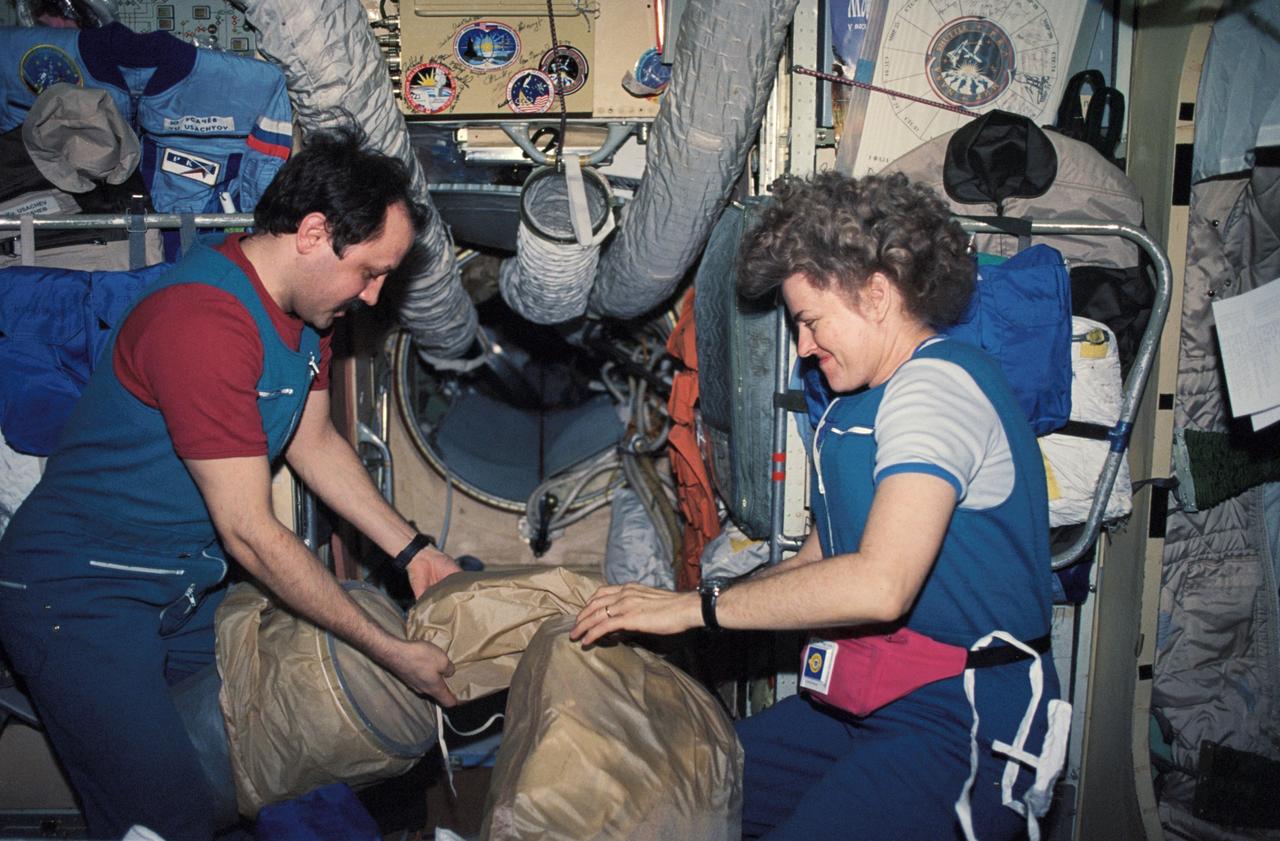 NM21-386-024 (March 1996) --- Onboard the Base Block Module of Russia&#0146;s Mir Space Station, as two members of the Mir-21 crew prepare to move supplies to their proper stowage places.  Astronaut Shannon W. Lucid, recently dropped off by the STS-76 Space Shuttle Atlantis crew members and now serving as a cosmonaut guest researcher, works with Yury V. Usachev, flight engineer.  She went on to spend a total of 188 consecutive days in space before returning to Earth with the STS-79 crew.  She worked with a total of five cosmonauts at various times during that stay.