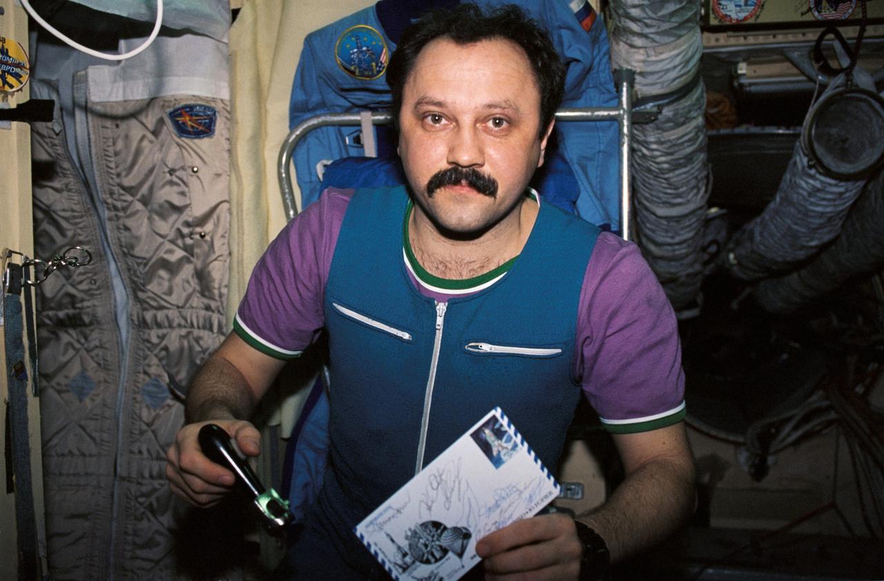 NM21-397-034 (For Release October 1996) --- Cosmonaut Yury V. Usachev, Mir 21 flight engineer, holds a peeler and a piece of mail received along with the food in the Base Block module of the Mir Space Station.