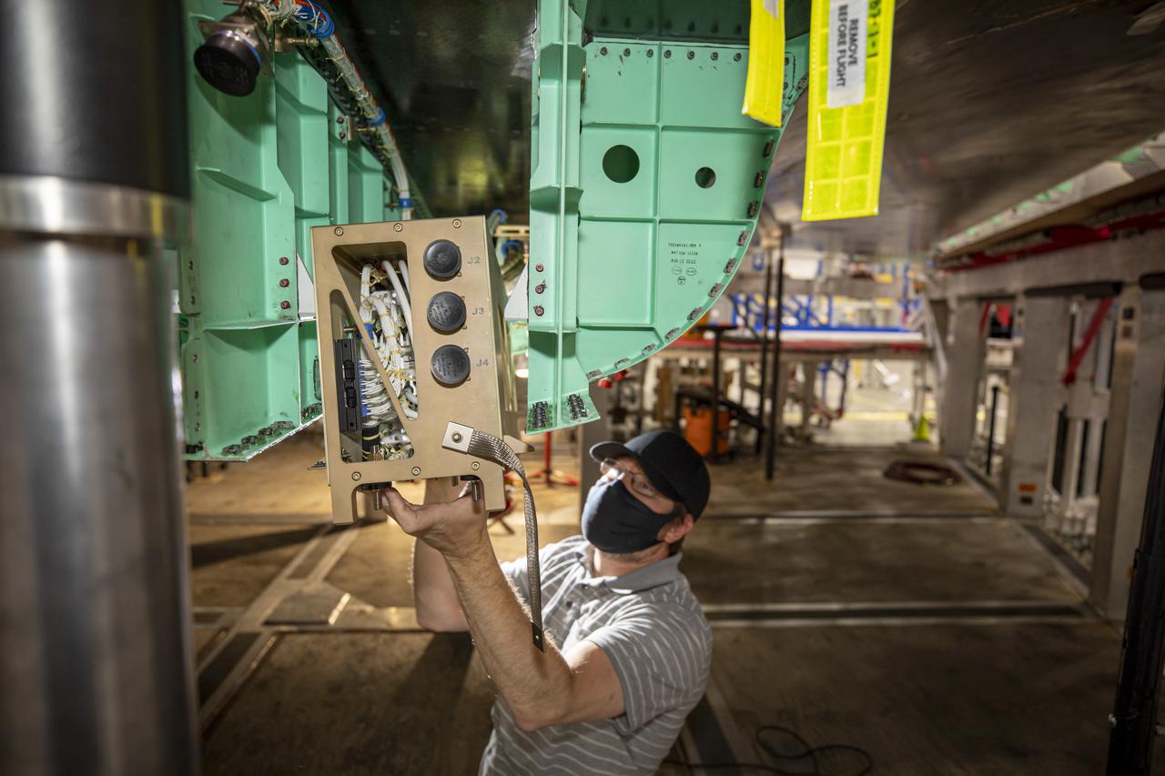 A technician works on the installation of the PDS Pallet (gold colored box that he is holding) on NASA’s X-59 Quiet SuperSonic Technology or QueSST aircraft.  Lockheed Martin Photography By Garry Tice 1011 Lockheed Way, Palmdale, Ca. 93599 Event: SEG 450 Mid Bay - PDS Fit Check Date: 5/03/2021