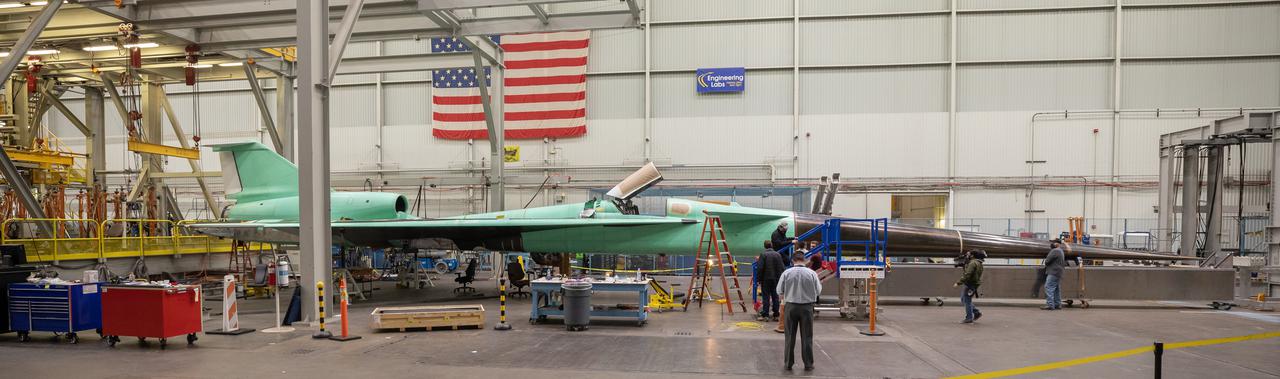 This panoramic side view of NASA’s X-59 Quiet SuperSonic Technology airplane shows the aircraft sitting on jacks at a Lockheed Martin test facility in Fort Worth, Texas.  Lockheed Martin Aeronautics Company - Fort Worth - Chris Hanoch Subject: SEG 230 Nose Attachement FP#: 21-03420 POC: Analiese Smith, Chris Higgins Other info: X-59 in Fort Worth, testing
