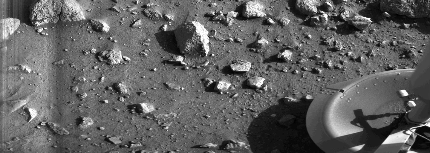This is the first photograph ever taken on the surface of the planet Mars. It was obtained by Viking 1 just minutes after the spacecraft landed successfully early today [July 20, 1976]. The center of the image is about 1.4 meters (five feet) from Viking Lander camera #2. We see both rocks and finely granulated material--sand or dust. Many of the small foreground rocks are flat with angular facets. Several larger rocks exhibit irregular surfaces with pits and the large rock at top left shows intersecting linear cracks. Extending from that rock toward the camera is a vertical linear dark band which may be due to a one-minute partial obscuration of the landscape due to clouds or dust intervening between the sun and the surface. Associated with several of the rocks are apparent signs of wind transport of granular material. The large rock in the center is about 10 centimeters (4 inches) across and shows three rough facets. To its lower right is a rock near a smooth portion of the Martian surface probably composed of very fine-grained material. It is possible that the rock was moved during Viking 1 descent maneuvers, revealing the finer-grained basement substratum; or that the fine-grained material has accumulated adjacent to the rock. There are a number of other furrows and depressions and places with fine-grained material elsewhere in the picture. At right is a portion of footpad #2. Small quantities of fine grained sand and dust are seen at the center of the footpad near the strut and were deposited at landing. The shadow to the left of the footpad clearly exhibits detail, due to scattering of light either from the Martian atmosphere or from the spacecraft, observable because the Martian sky scatters light into shadowed areas.  http://photojournal.jpl.nasa.gov/catalog/PIA00381