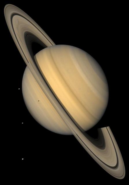 This approximate natural-color image shows Saturn, its rings, and four of its icy satellites. Three satellites (Tethys, Dione, and Rhea) are visible against the darkness of space, and another smaller satellite (Mimas) is visible against Saturn's cloud tops very near the left horizon and just below the rings. The dark shadows of Mimas and Tethys are also visible on Saturn's cloud tops, and the shadow of Saturn is seen across part of the rings. Saturn, second in size only to Jupiter in our Solar System, is 120,660 km (75,000 mi) in diameter at its equator (the ring plane) but, because of its rapid spin, Saturn is 10% smaller measured through its poles. Saturn's rings are composed mostly of ice particles ranging from microscopic dust to boulders in size. These particles orbit Saturn in a vast disk that is a mere 100 meters (330 feet) or so thick. The rings' thinness contrasts with their huge diameter--for instance 272,400 km (169,000 mi) for the outer part of the bright A ring, the outermost ring visible here. The pronounced concentric gap in the rings, the Cassini Division (named after its discoverer), is a 3500-km wide region (2200 mi, almost the width of the United States) that is much less populated with ring particles than the brighter B and A rings to either side of the gap. The rings also show some enigmatic radial structure ('spokes'), particularly at left. This image was synthesized from images taken in Voyager's blue and violet filters and was processed to recreate an approximately natural color and contrast.  http://photojournal.jpl.nasa.gov/catalog/PIA00400