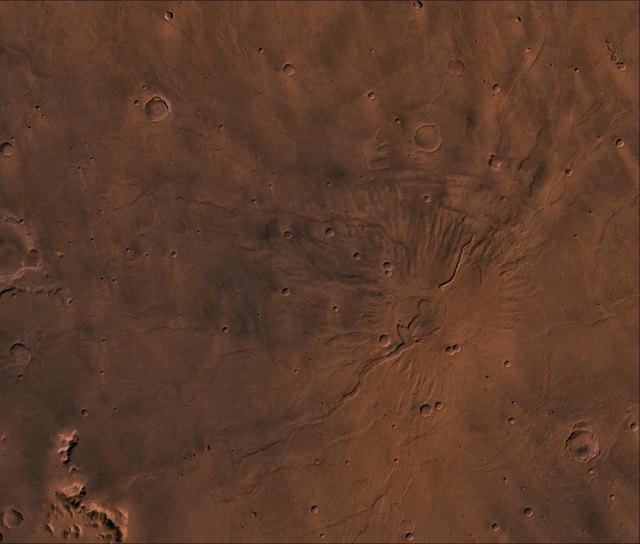 A color image of the Tyrrhena Patera Region of Mars; north toward top. The scene shows a central circular depression surrounded by circular fractures and highly dissected horizontal sheets. A patera (Latin for shallow dish or saucer) is a volcano of broad areal extent with little vertical relief. This image is a composite of Viking medium-resolution images in black and white and low-resolution images in color. The image extends from latitude 17 degrees S. to 25 degrees S. and from longitude 250 degrees to 260 degrees; Mercator projection.  Tyrrhena Patera has a 12-km-diameter caldera at its center surrounded by a 45-km-diameter fracture ring. Around the fracture ring, the terrain is highly eroded forming ragged outward-facing cliffs, as though successive flat-lying layers had been eroded back. Cut into the sequence are several flat-floored channels that extend outward as far as 200 km from the center of the volcano. The structure may be composed of highly erodible ash layers and the channels may be fluvial, with the release of water being triggered by volcanic activity (Carr, 1981, The surface of Mars, Yale Univ. Press, New Haven, 232 p.).   http://photojournal.jpl.nasa.gov/catalog/PIA00421