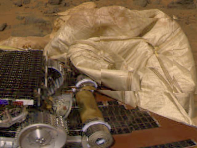 This image from the Imager for Mars Pathfinder (IMP) camera shows the rear part of the Sojourner rover, the rolled-up rear ramp, and portions of the partially deflated airbags. The Alpha Proton X-ray Spectrometer instrument is protruding from the rear (right side) of the rover. The airbags behind the rover are presently blocking the ramp from being safely unfurled. The ramps are a pair of deployable metal reels that will provide a track for the rover as it slowly rolls off the lander, and onto the surface of Mars, once Pathfinder scientists determine it is safe to do so.  http://photojournal.jpl.nasa.gov/catalog/PIA00614