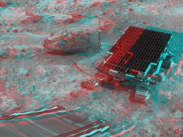 At right, NASA Sojourner has traveled off the lander rear ramp and onto the surface of Mars. The rock Barnacle Bill and the rear ramp is to the left of Sojourner. 3D glasses are necessary to identify surface detail.   
