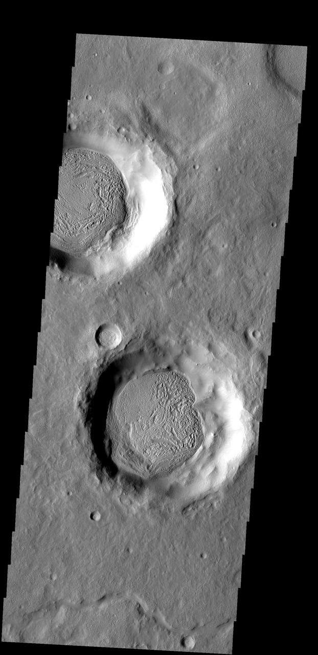 The material covering the floors of these two craters looks very different from the surrounds. The unusual markings of the floor material indicates that a volatile, such as ice, has affected the appearance of the surface