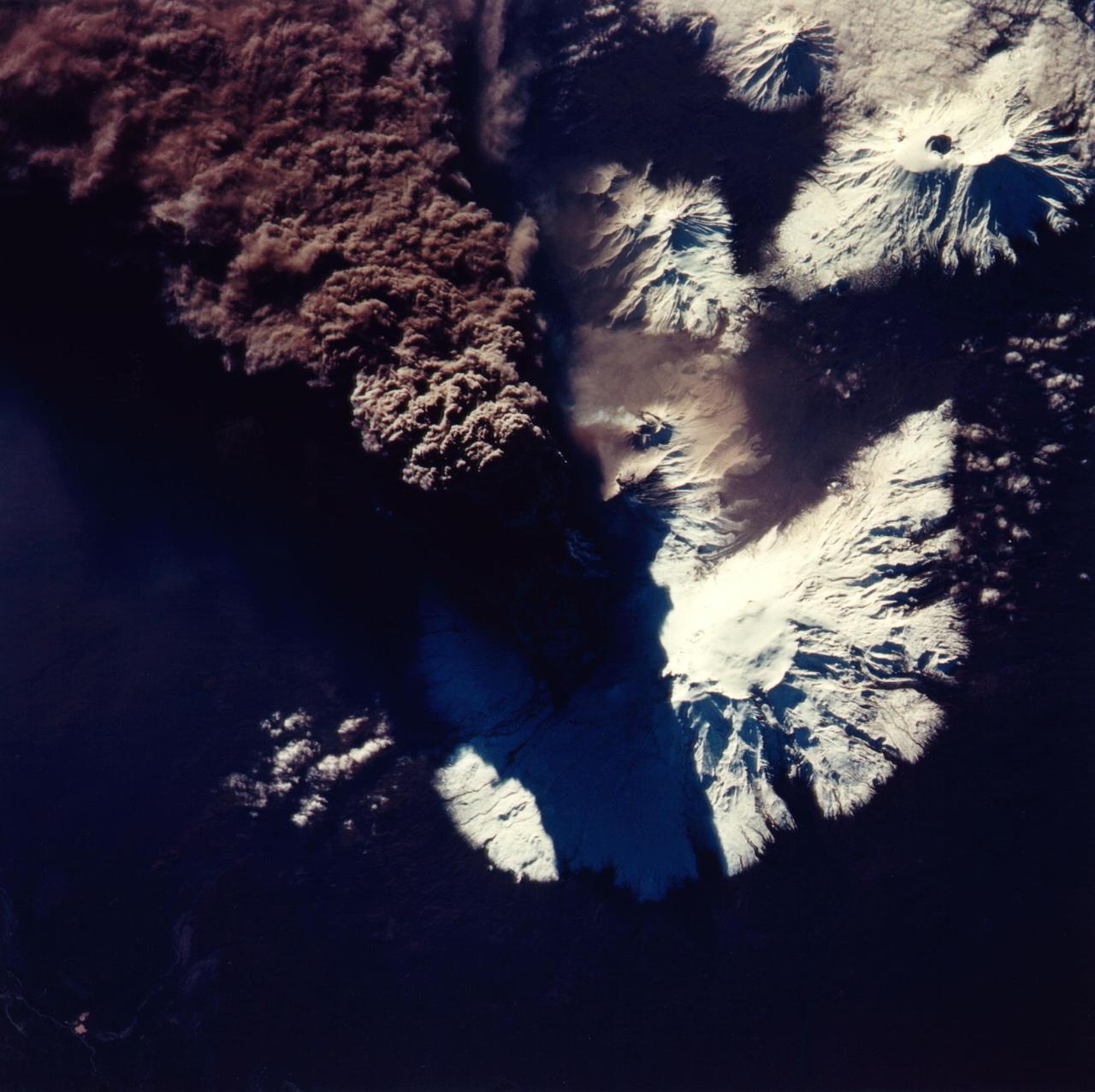 This photograph of the eruption of Kliuchevskoi volcano, Kamchatka, Russia was taken by space shuttle Endeavour astronauts during the early hours of the eruption on September 30, 1994. The ash plume, which reached heights of more than 18 kilometers (50,000 feet), is emerging from a vent on the north flank of Kliuchevskoi, partially hidden by the plume and its shadow in this view. The photograph is oriented with north toward the bottom, for comparison with the Spaceborne Imaging Radar C/X-Band Synthetic Aperture Radar (SIR-C/X-SAR) image (P-44823) that was acquired a few days later. Near the center of the photo, a small whitish steam plume may be seen emanating from the growing lava dome of a companion volcano, Bezymianny. http://photojournal.jpl.nasa.gov/catalog/PIA01766