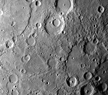 NASA Mariner 10 photo reveals a heavily cratered terrain on Mercury with a prominent scrap extending several hundred kilometers across the upper left. A crater, nested in a larger crater, is at top center. 