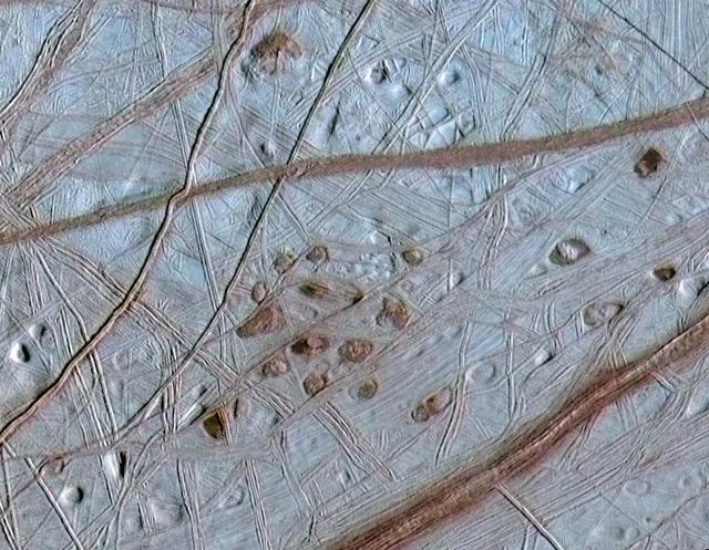 Reddish spots and shallow pits pepper the enigmatic ridged surface of Europa in this view combining information from images taken by NASA Galileo spacecraft during two different orbits around Jupiter.