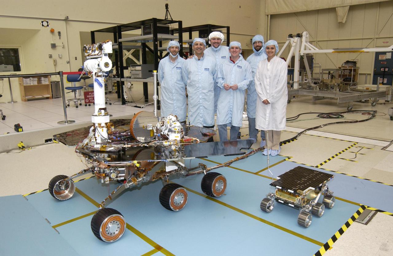 Members of the Mars Exploration Rovers Assembly, Test and Launch Operations team gather around NASA Rover 2 and its predecessor, a flight spare of the Pathfinder mission Sojourner rover, named Marie Curie.