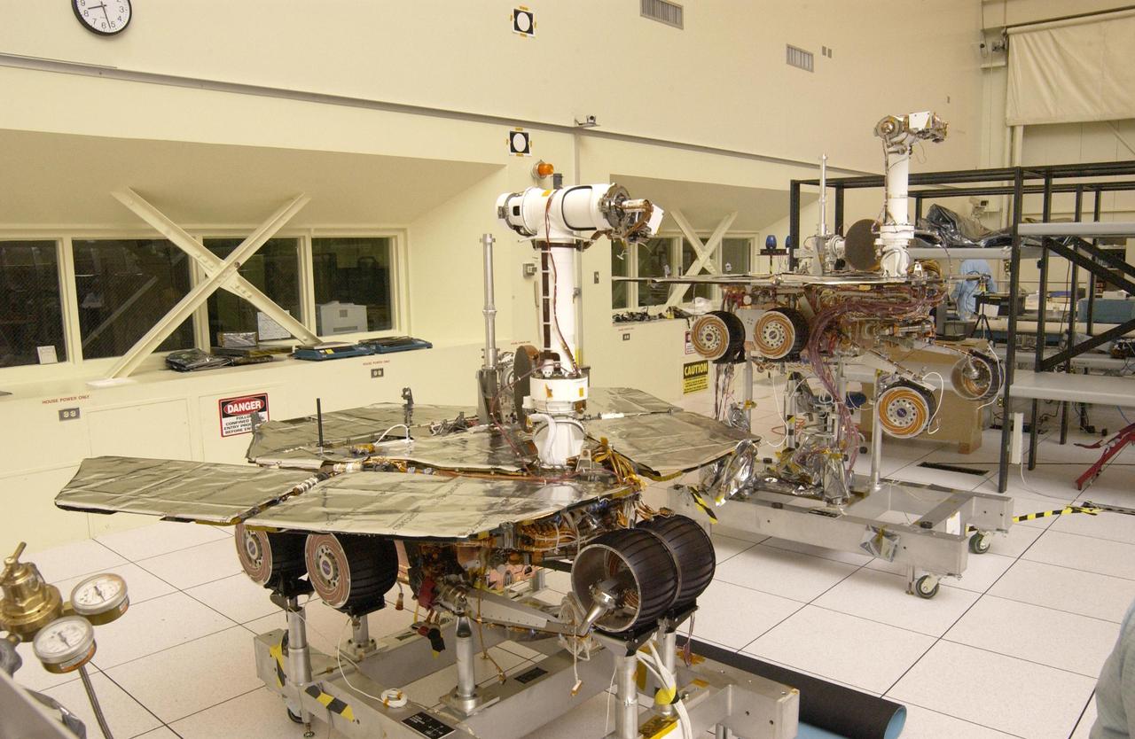 The twin rovers sit side-by-side in different stages of deployment. NASA Rover 2 left front wheels are stowed, while NASA Rover 1 front wheels are deployed.