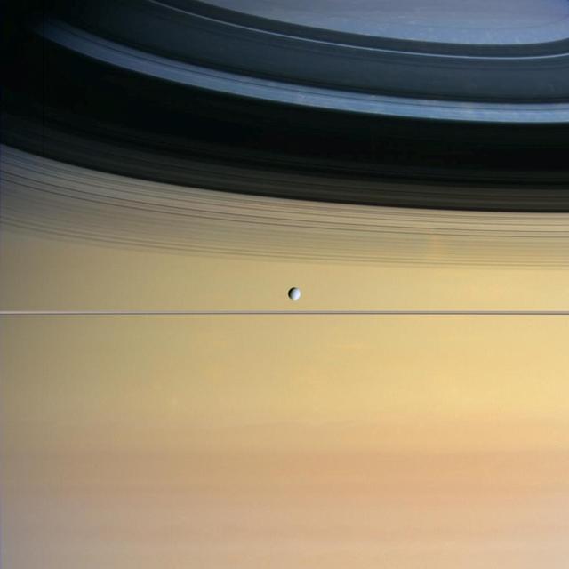 Cool and icy Dione floats in front of giant Saturn bedecked in a dazzling array of colors