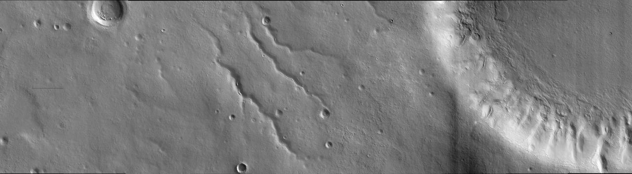 This image was taken in the mid-latitudes of Mars' southern hemisphere near the giant Argyre impact basin. It is located just to the west of a prominent scarp known as Bosporos Rupes. The left side of the image shows cratered plains. Some of the craters are heavily mantled and indistinct, whereas others exhibit sharp rims and dramatic topography. The largest crater in this half of the image is about 2.5 kilometers (1.5 miles) wide. Mounds and ridges, which may be remnants of an ice-rich deposit, are visible on its floor. Three sinuous valleys occupy the center of the image. Valleys such as these were first observed in data returned by the NASA Mariner 9 spacecraft, which reached Mars in 1971. The right side of the image shows part of an impact crater that is approximately 20 kilometers (12 miles) in diameter. The furrowed appearance of the crater's inner wall suggests that it has been extensively modified, perhaps by landslides and flowing water. Like other craters in the area, the floor of this crater has a rough and dissected texture that is often attributed to the loss of ice-rich material.  This image was taken by the High Resolution Imaging Science Experiment (HiRISE) camera onboard NASA's Mars Reconnaissance Orbiter spacecraft on March 24, 2006. The image is centered at 40.64 degrees south latitude, 303.49 degrees east longitude. The image is oriented such that north is 7 degrees to the left of up. The range to the target was 2,044 kilometers (1,270 miles). At this distance the image scale is 2.04 meters (6.69 feet) per pixel, so objects as small as 6.1 meters (20 feet) are resolved. In total this image is 40.90 kilometers (25.41 miles) or 20,081 pixels wide and 11.22 kilometers (6.97 miles) or 5,523 pixels high. The image was taken at a local Mars time of 07:30 and the scene is illuminated from the upper right with a solar incidence angle of 81.4 degrees, thus the sun was about 8.6 degrees above the horizon. At an Ls of 29 degrees (with Ls an indicator of Mars' position in its orbit around the sun), the season on Mars is southern autumn.  http://photojournal.jpl.nasa.gov/catalog/PIA08047