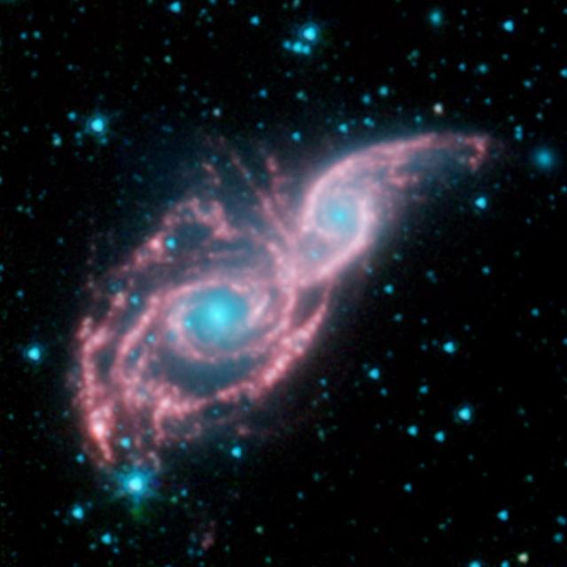 Something appears to be peering through a shiny red mask, in this new false-colored image from NASA Spitzer Space Telescope. The mysterious blue eyes are actually starlight from the cores of two merging galaxies, called NGC 2207 and IC 2163.