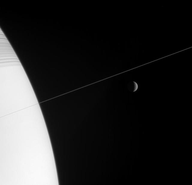 Shadow-striped Saturn and its exquisitely thin rings occupy the near field  in this Cassini spacecraft view, while a crescent Rhea hangs in the  distance