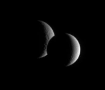 Dione and Rhea pair up for an occultation, or mutual event, as seen by  Cassini. While the lit portion of each moon is but a crescent, the dark  side of Dione has begun to take a bite out of its distant sibling moon