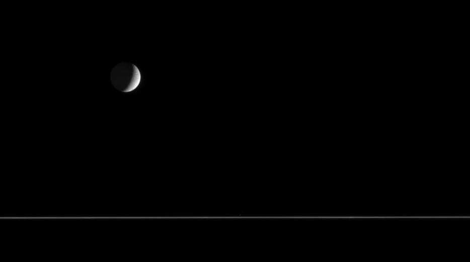 Quiet and cold, a crescent Tethys floats above the nearly edge-on rings of  Saturn. The only surface features visible on Tethys 1,071 kilometers, or  665 miles across from this distance are a few impact craters