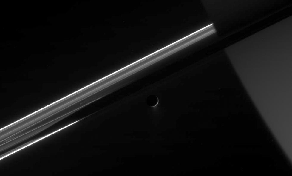 Cassini stares toward the night side of Saturn, seen here on the right, as  the active icy moon Enceladus glides past