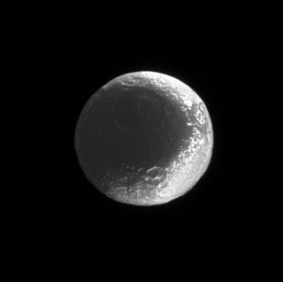 This Cassini spacecraft view shows how the bright and dark regions on Iapetus fit together like the seams of a baseball. Some of the material that covers the moon dark, leading side spills over into regions on the brighter trailing side