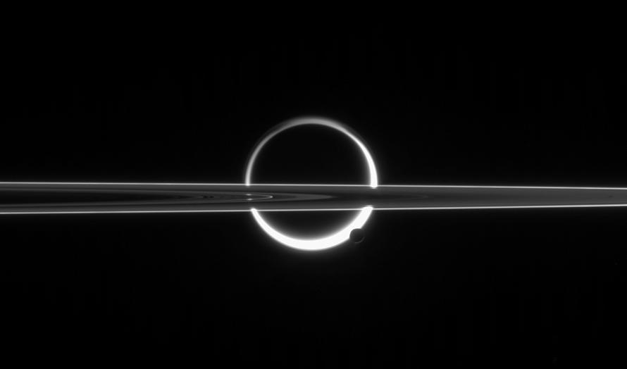 Saturn rings cut across an eerie scene that is ruled by Titan luminous crescent and globe-encircling haze, broken by the small moon Enceladus, whose icy jets are dimly visible at its south pole. North is up