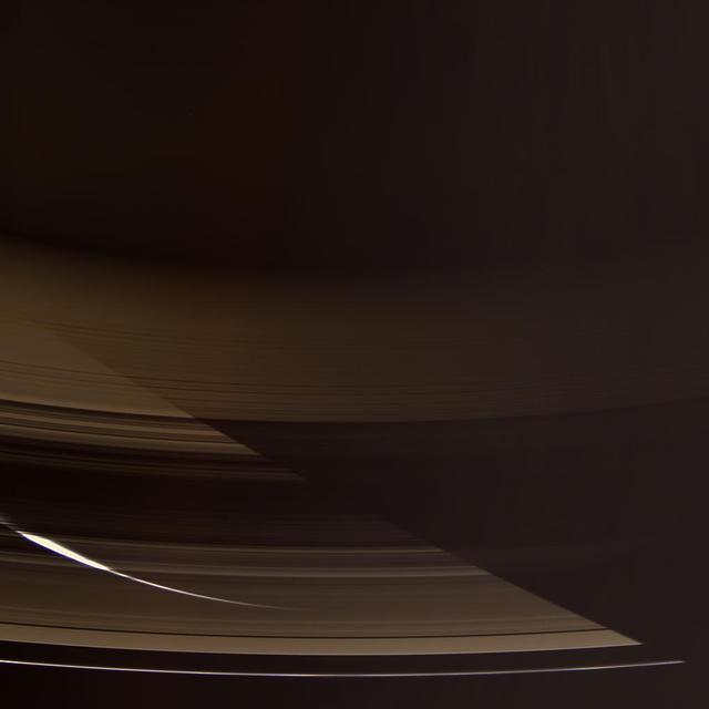 The Cassini spacecraft gazes down through the dark side of Saturn rings toward the softly glowing planet. The night side southern hemisphere is lit by sunlight reflecting off the opposite side of the rings
