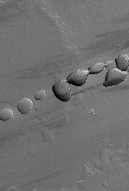 This MOC image shows a portion of a chain of pits on a lava- and dust-covered plain northwest of Tharsis Tholus, one of the many volcanic constructs in the Tharsis region of Mars
