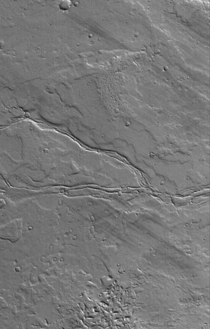 This MOC image shows the remains of leveed lava channels cutting across west to east a dust-covered plain composed of overlapping lava flows east of Olympus Mons