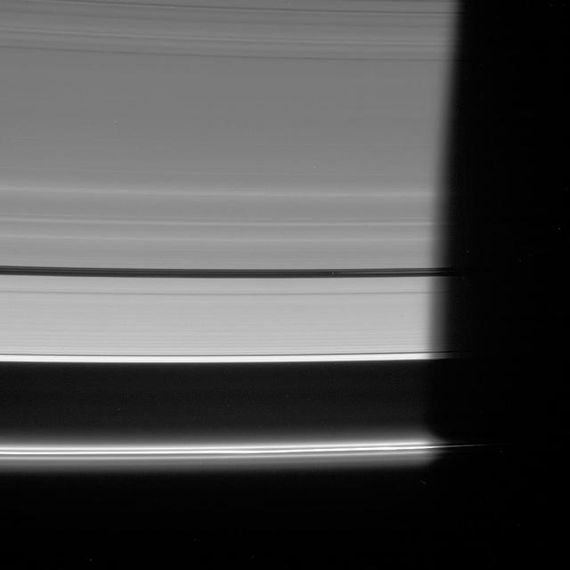 NASA Cassini spacecraft looks down at the unlit side of the rings as Pan heads into Saturn shadow. The moon is accompanied by faint ringlets in the Encke Gap.