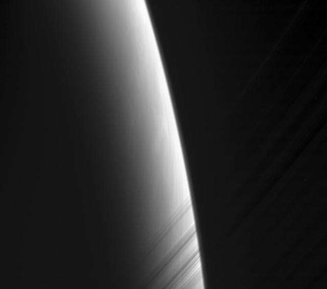 The Cassini spacecraft looks toward daybreak on Saturn through the delicate strands of the C ring. Some structure and contrast is visible in the clouds far below