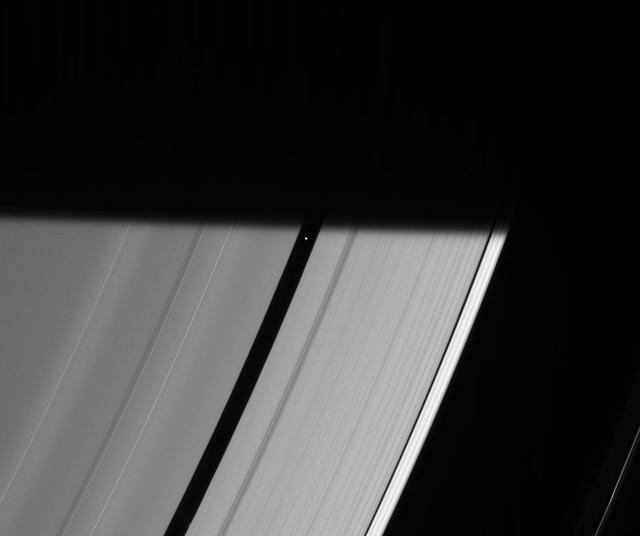 Pan prepares to be engulfed by the darkness of Saturn shadow, visible here as it stretches across the rings