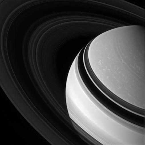 Held in gravity embrace, Saturn darkened, icy rings encircle the clouded gas giant