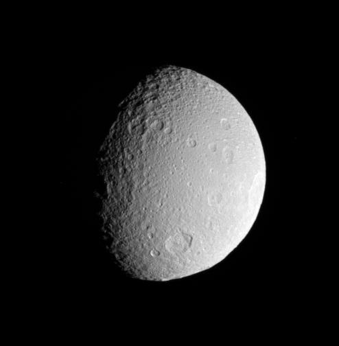 The Cassini spacecraft surveys the battered surface of icy Tethys. The great impact basin straddling the terminator is itself overprinted by many smaller impact sites