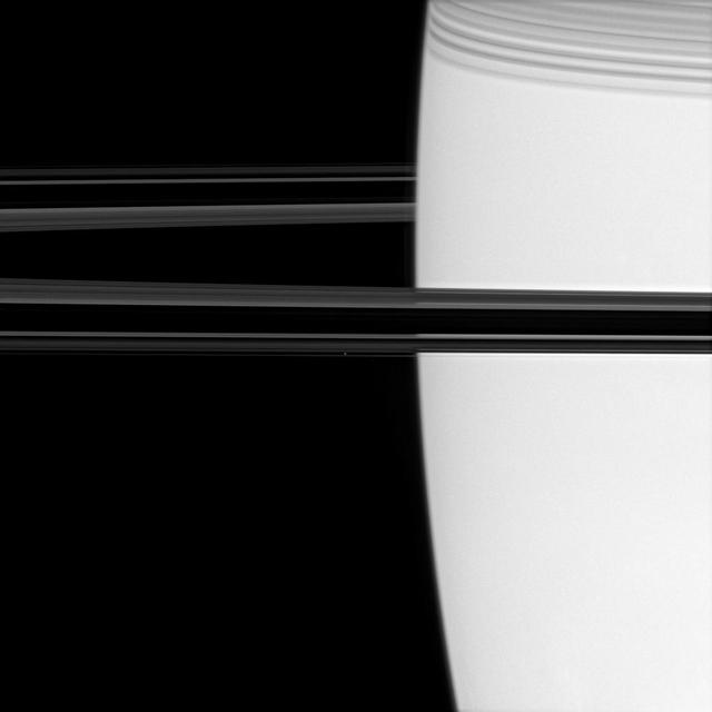 Off the shoulder of giant Saturn, a bright pinpoint marks the location of the ring moon Atlas image center. Shadows cast by the C ring adorn the planet at upper right